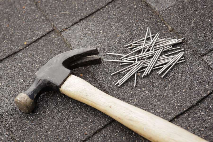 A hammer and nails resting on a roof represent tools for roof maintenance in South Florida.
